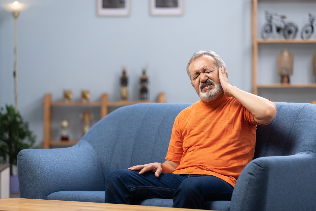 Senior man with ear pain sitting on sofa at home