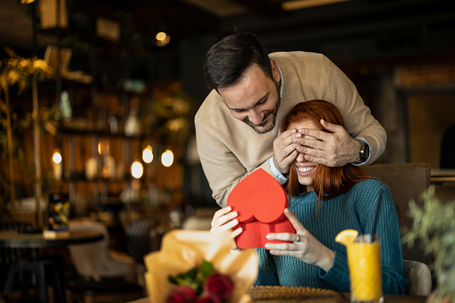 Man surprising his girlfriend with a heart-shaped box on valentine's day.